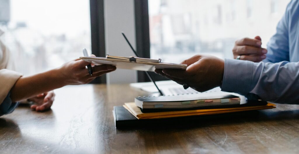 pexels-photo-5673502-5673502 Crop anonymous ethnic woman passing clipboard to office worker with laptop during job interview